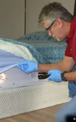 How to treat bed bugs at home: man inspecting a box spring with a flashlight